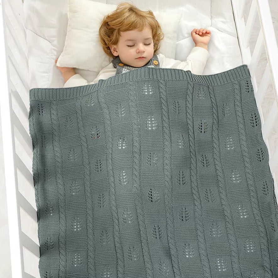 Child sleeping under a textured green blanket in a crib