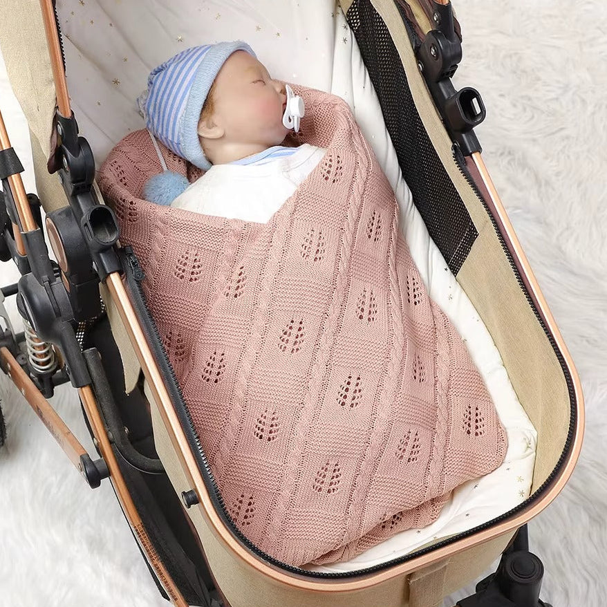 Baby wrapped in a pink knitted blanket inside a stroller on a white background