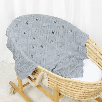 Gray textured blanket draped over a wooden Moses basket on a white background