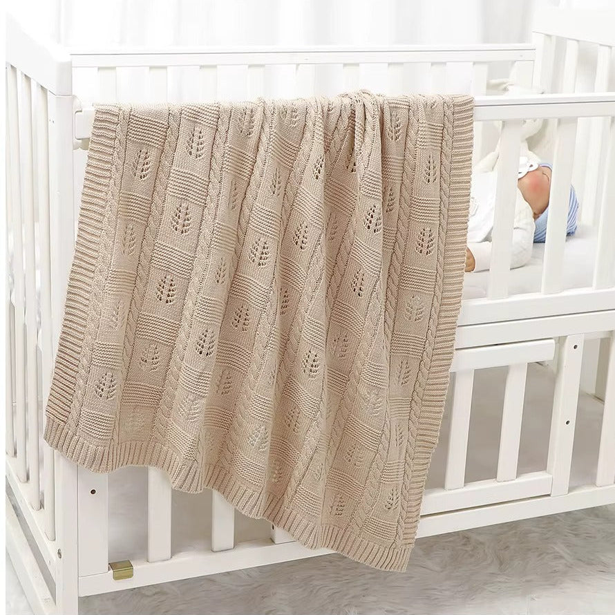 Beige textured blanket draped over a white crib with a baby partially visible.