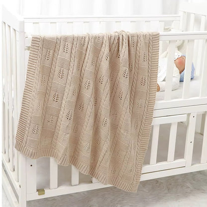 Beige textured blanket draped over a white crib with a baby partially visible.