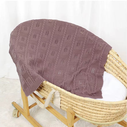 Knitted purple blanket draped over a wooden Moses basket on a white background