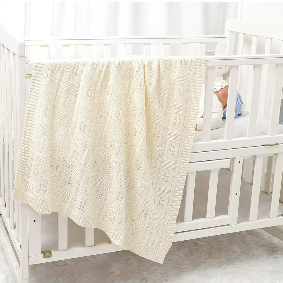 White crib with a textured white blanket draped over the side, baby partially visible.