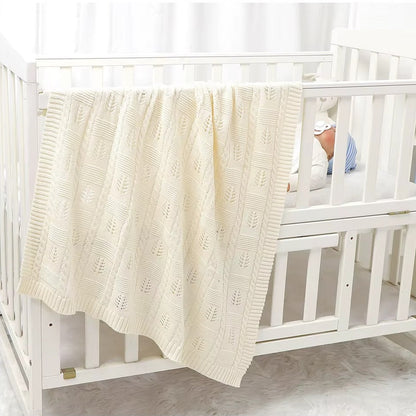 White crib with a textured white blanket draped over the side, baby partially visible.