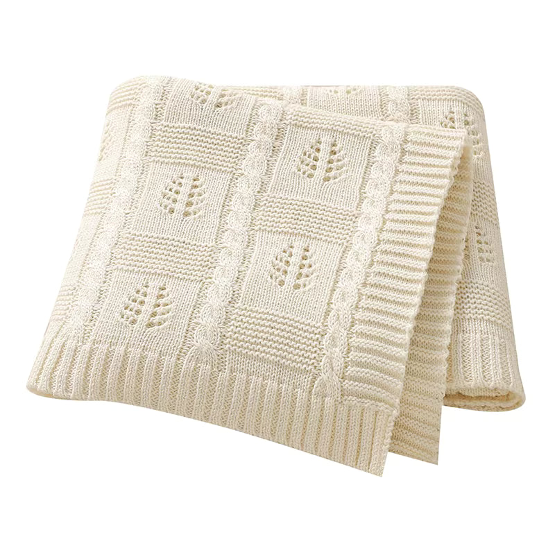 Folded cream-colored knitted blanket with a subtle pattern on a white background