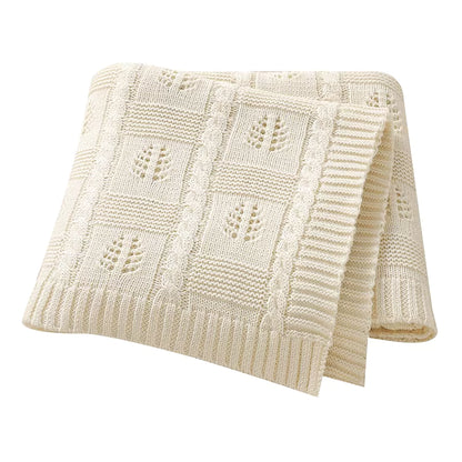 Folded cream-colored knitted blanket with a subtle pattern on a white background