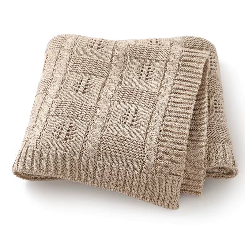 Folded oatmeal-colored knitted blanket with a subtle pattern on a white background
