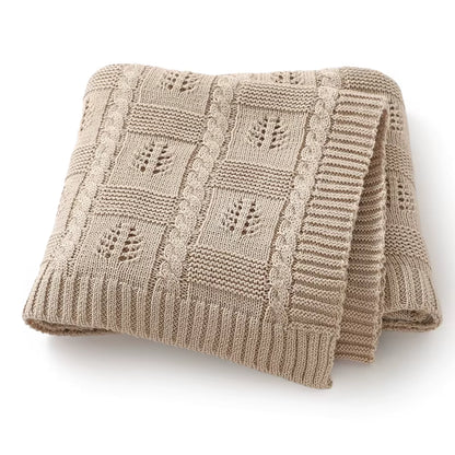 Folded oatmeal-colored knitted blanket with a subtle pattern on a white background