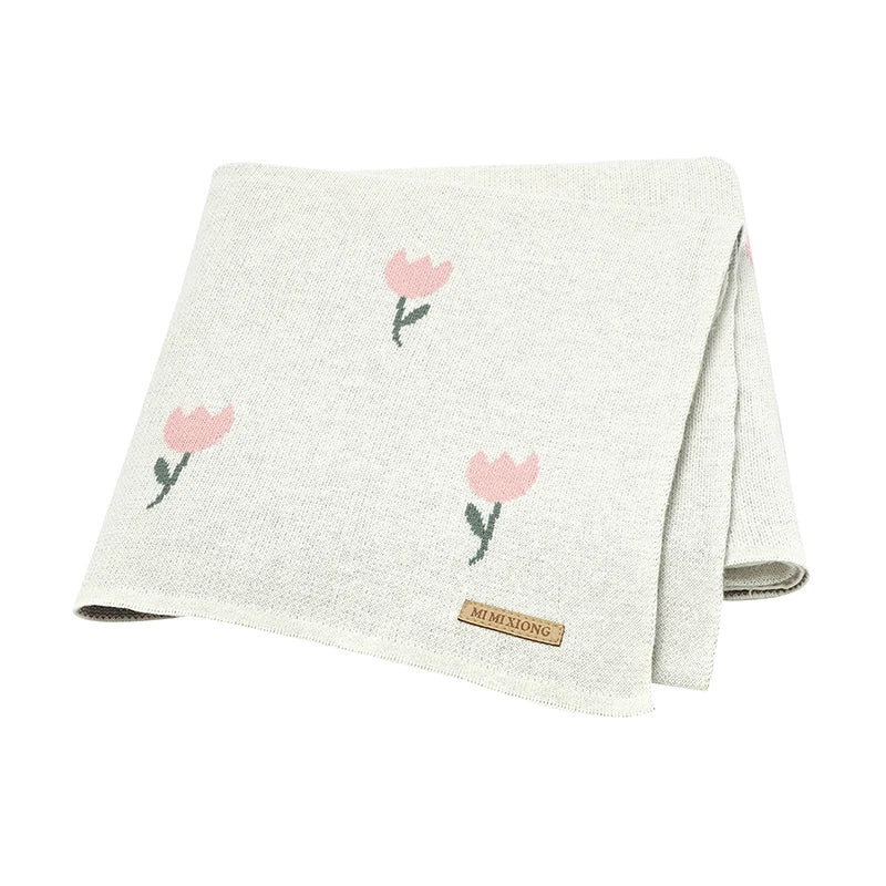 An ivory white cotton knit baby blanket with a soft pink woven tulip pattern, folded flat on a white background.