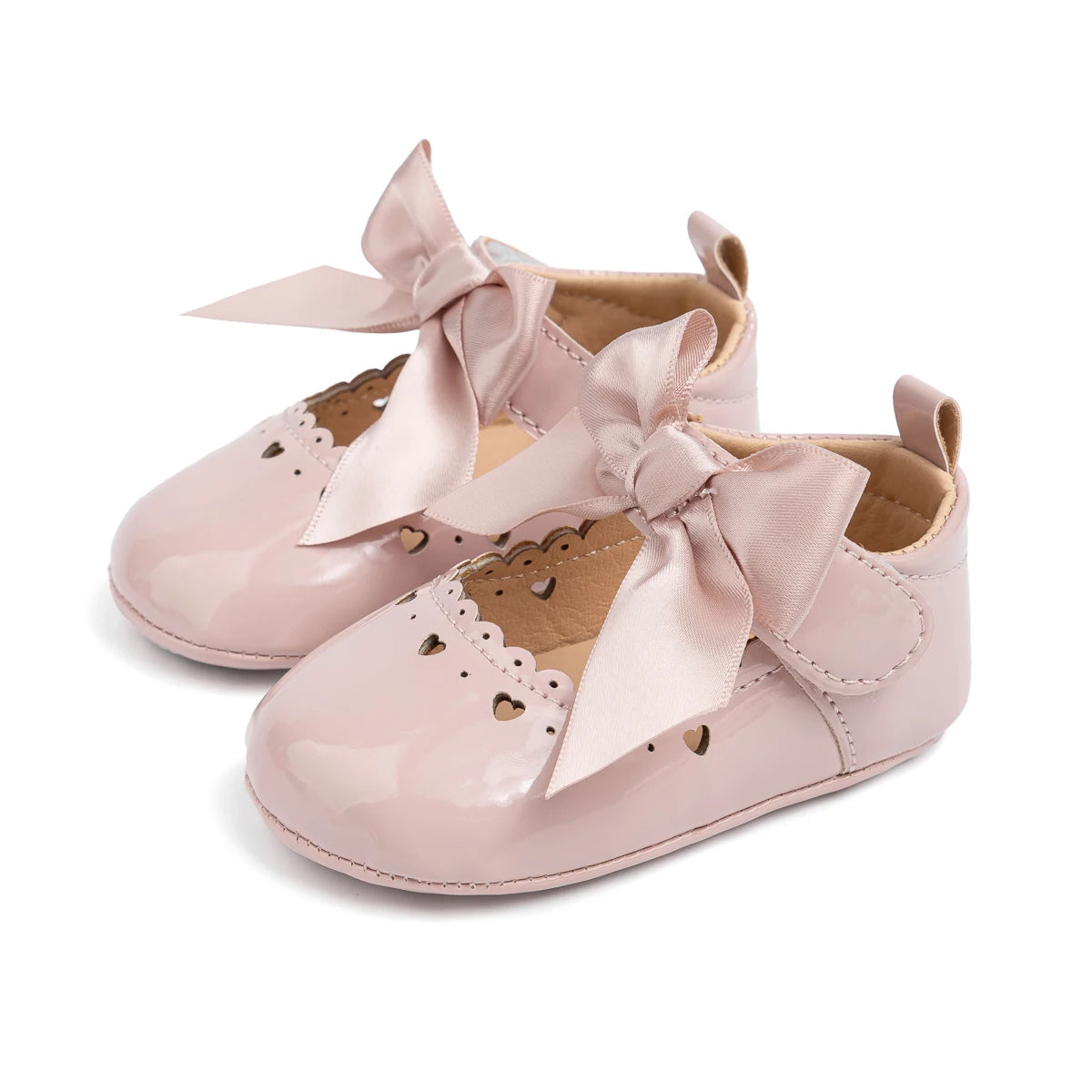Pair of soft pink PU leather infant Mary Jane dress shoes with a matching satin bow and heart cutouts.
