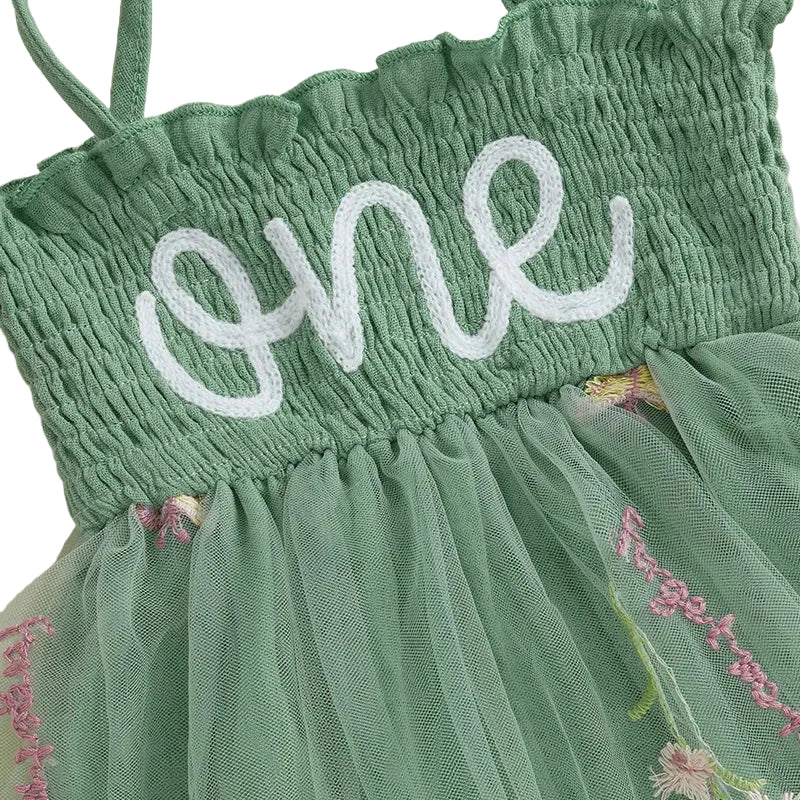 Close-up of the high-quality white chain-stitch "one" embroidery on the comfortable green smocked bodice and floral tulle layers.