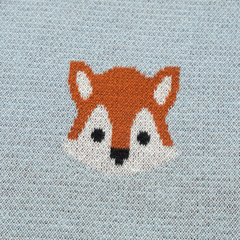 Detailed close-up of knitted orange fox face motif on light blue cotton baby blanket