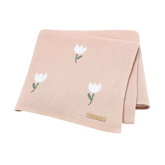 Premium blush pink 100% cotton knit baby blanket featuring a white woven tulip pattern, neatly folded to show the soft texture and brand accent tag.