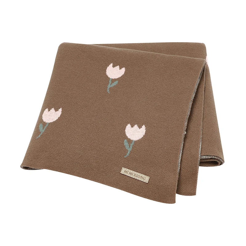 An earth-toned cocoa brown cotton knit baby blanket with a contrasting white woven tulip pattern, folded flat.
