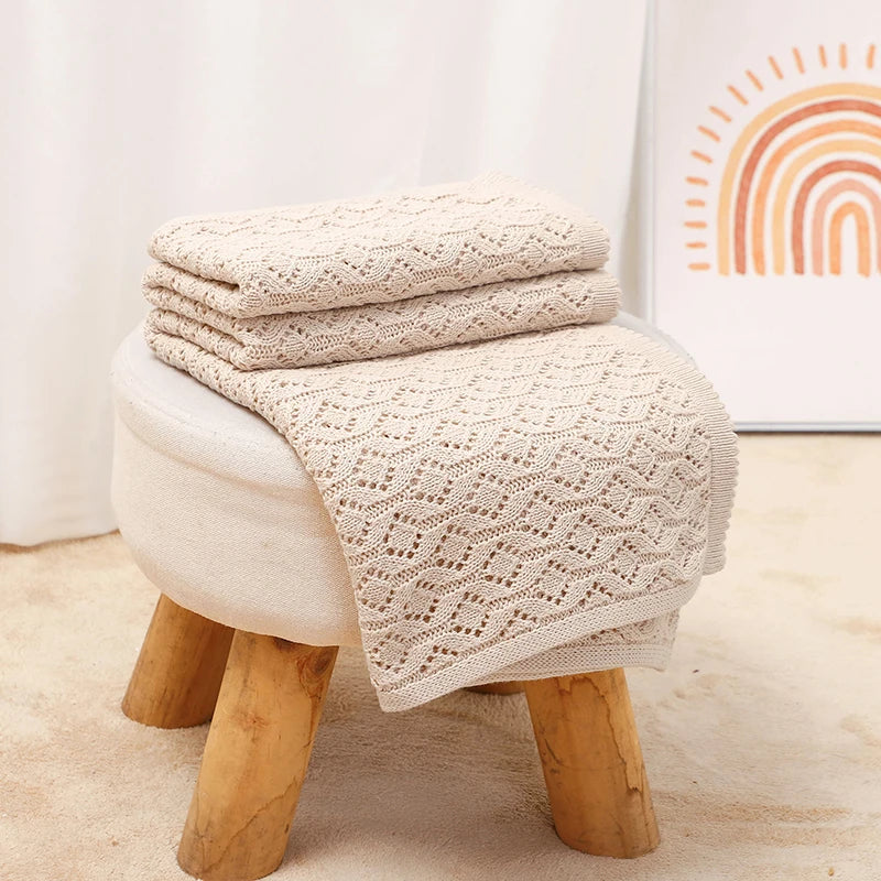Neatly folded oatmeal knitted cotton baby blanket resting on a nursery footstool