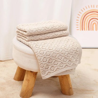 Neatly folded oatmeal knitted cotton baby blanket resting on a nursery footstool