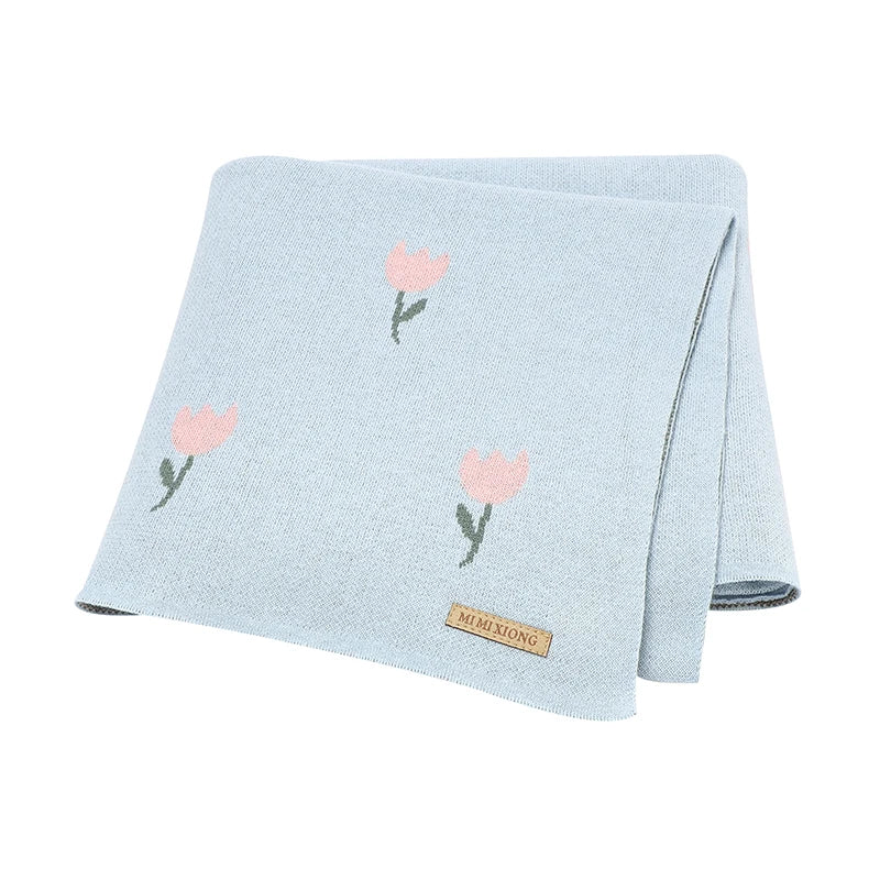 A powder blue 100% cotton knit baby blanket with a delicate pink woven tulip design, folded for display.