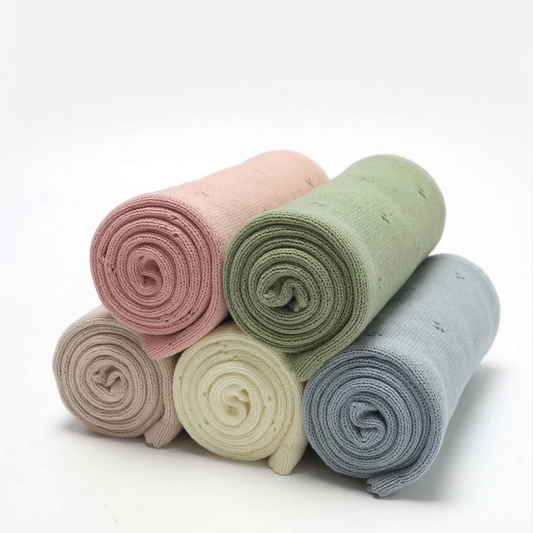 Stack of rolled-up 100% cotton pointelle baby blankets in pastel colors on a white background