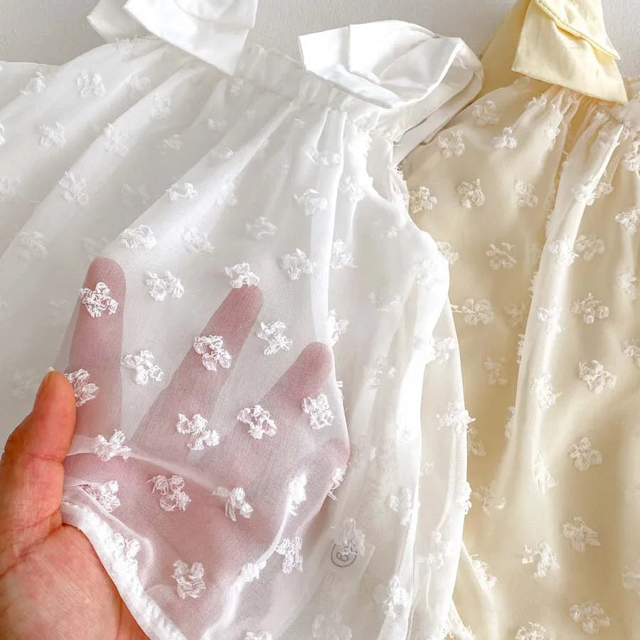 Close-up of sheer white 100% cotton gauze fabric showing the textured 3D Swiss dot floral pattern.