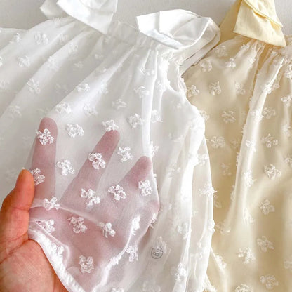 Close-up of sheer white 100% cotton gauze fabric showing the textured 3D Swiss dot floral pattern.