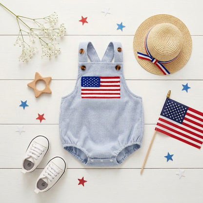 Flat lay view of the baby American flag bubble romper on a white background surrounded by a straw hat, shoes, star decorations, and a mini USA flag.