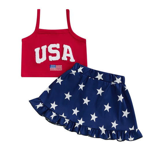Front view of a 4th of July toddler girl two-piece outfit featuring a sleeveless red tank top with a chenille embroidered USA patch and a navy blue skirt with white star prints and a ruffled hem.