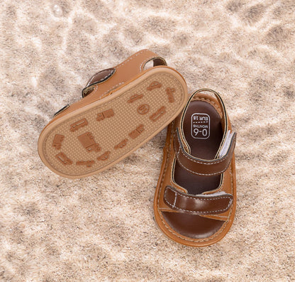 Bottom of brown baby sandals showing the anti-slip PVC sole with car and truck tread patterns.