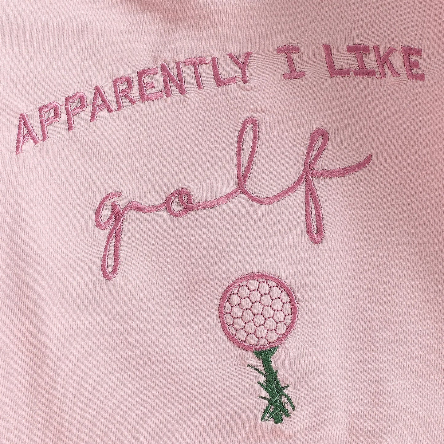 Close-up detail of the "Apparently I Like Golf" text and golf ball on a tee embroidery on the pink infant romper.