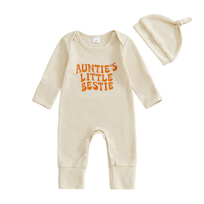Flat lay of a beige long-sleeve waffle knit baby romper with "Auntie's Little Bestie" embroidered in orange, alongside a matching infant knot hat.