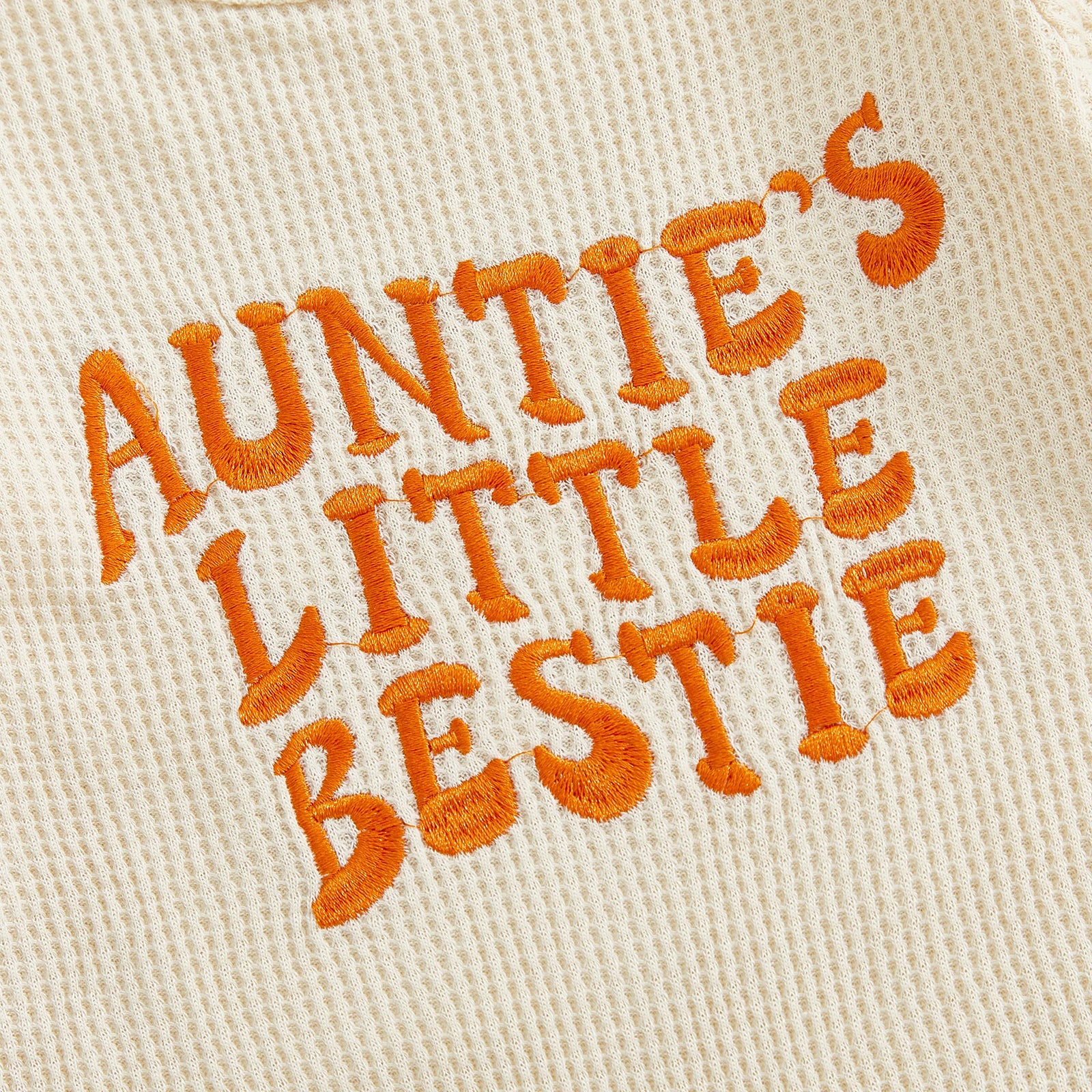 Close-up showing the premium orange textured embroidery of the words "Auntie's Little Bestie" on the beige waffle knit fabric.