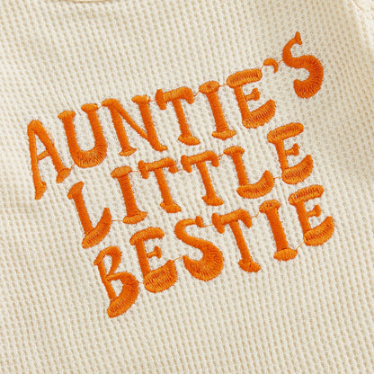 Close-up showing the premium orange textured embroidery of the words "Auntie's Little Bestie" on the beige waffle knit fabric.