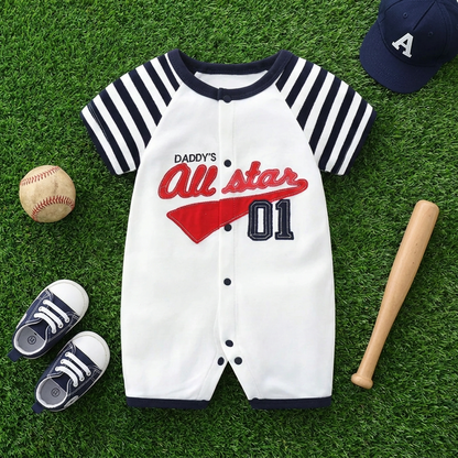 Flat lay of the baby boy baseball romper on artificial grass styled with a mini baseball bat, ball, shoes, and cap.