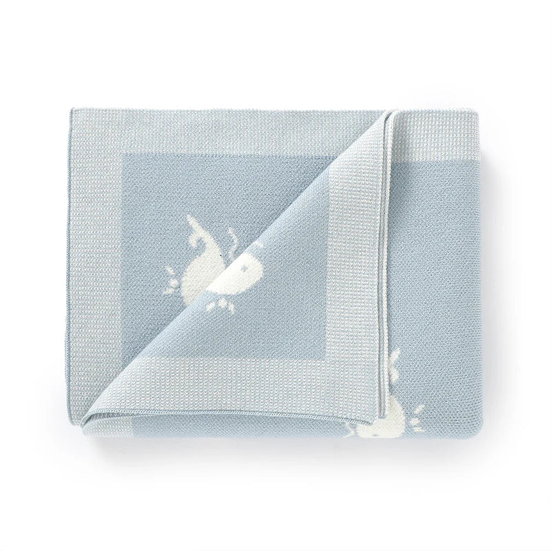 Flat folded Kidsely baby blue knit swaddle blanket featuring a cute ocean whale design