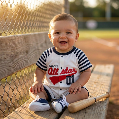 Smiling baby boy sitting on a wooden dugout bench at a baseball field during sunset, wearing the Daddy's All Star striped cotton romper, with a miniature wooden bat resting beside him.