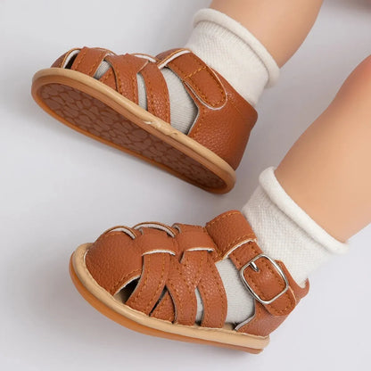 Brown closed-toe baby fisherman sandals worn with white socks on a model baby mannequin foot.