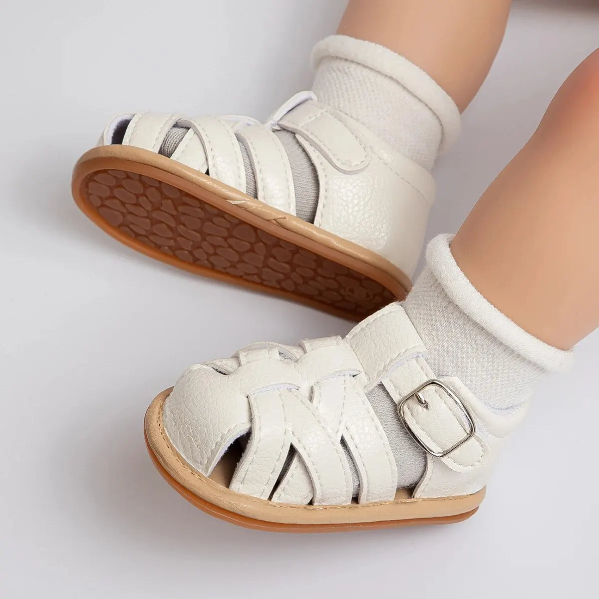 White closed-toe infant first walker sandals styled with white ankle socks on a baby model's feet.