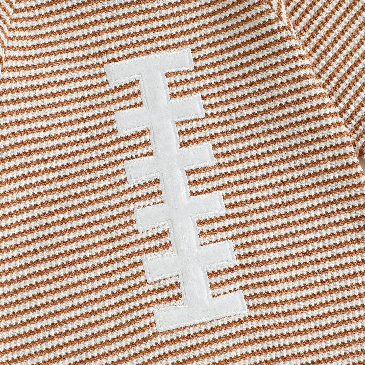 Close up of the white football laces applique and brown and white striped cotton blend fabric on the baby boy romper.