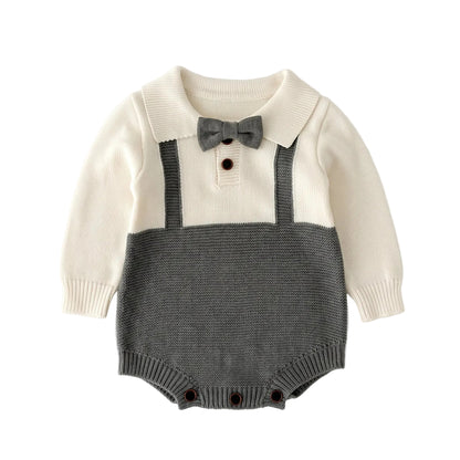 Flat lay of a baby boy formal knit romper featuring a cream top, gray faux suspenders, peter pan collar, and an attached bow tie.