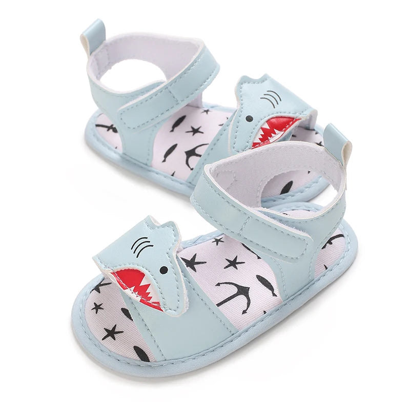 Angled view of light blue baby first walker sandals featuring a stitched shark face design.