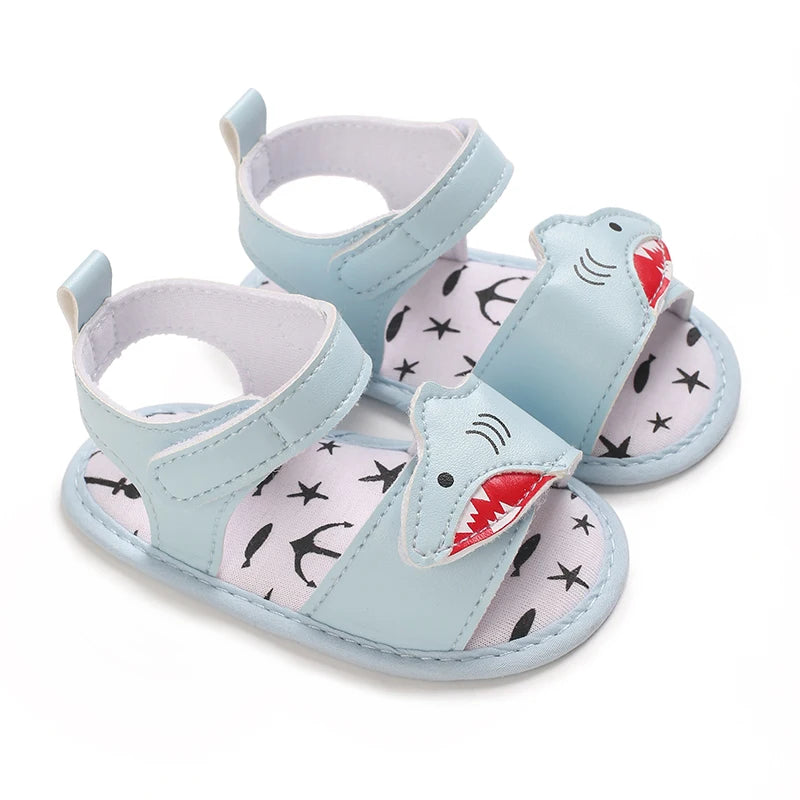 Pair of light blue baby boy shark sandals with a soft sole and nautical anchor and star print inside.