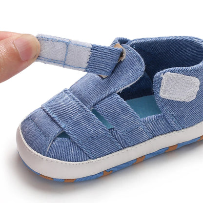 Close-up of a hand opening the adjustable velcro strap on a blue baby canvas summer sandal.