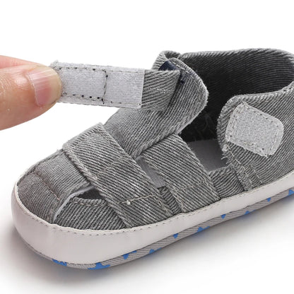 Close-up of a hand opening the adjustable velcro strap on a light gray baby canvas summer sandal.