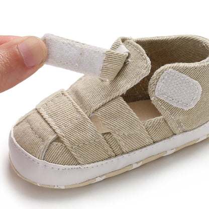 Close-up of a hand opening the adjustable velcro strap on a tan beige baby canvas summer sandal.