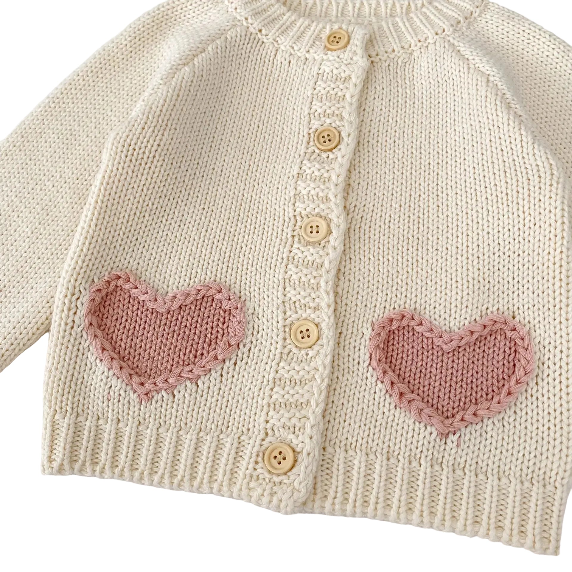 Detailed view of pink heart-shaped knit pockets on front of cream toddler sweater.