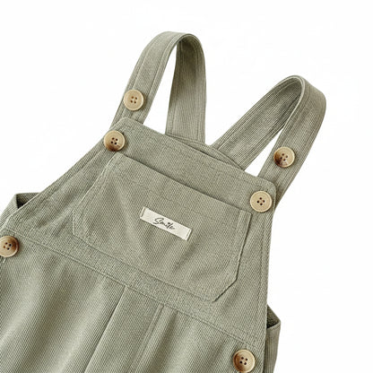 Close-up of button shoulder straps, front pocket, and cursive Smile chest tag on sage green corduroy overalls.