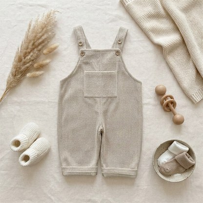 Flat lay of Kidsely beige ribbed corduroy baby overalls styled with white baby shoes, a wooden teething toy, and neutral decor.