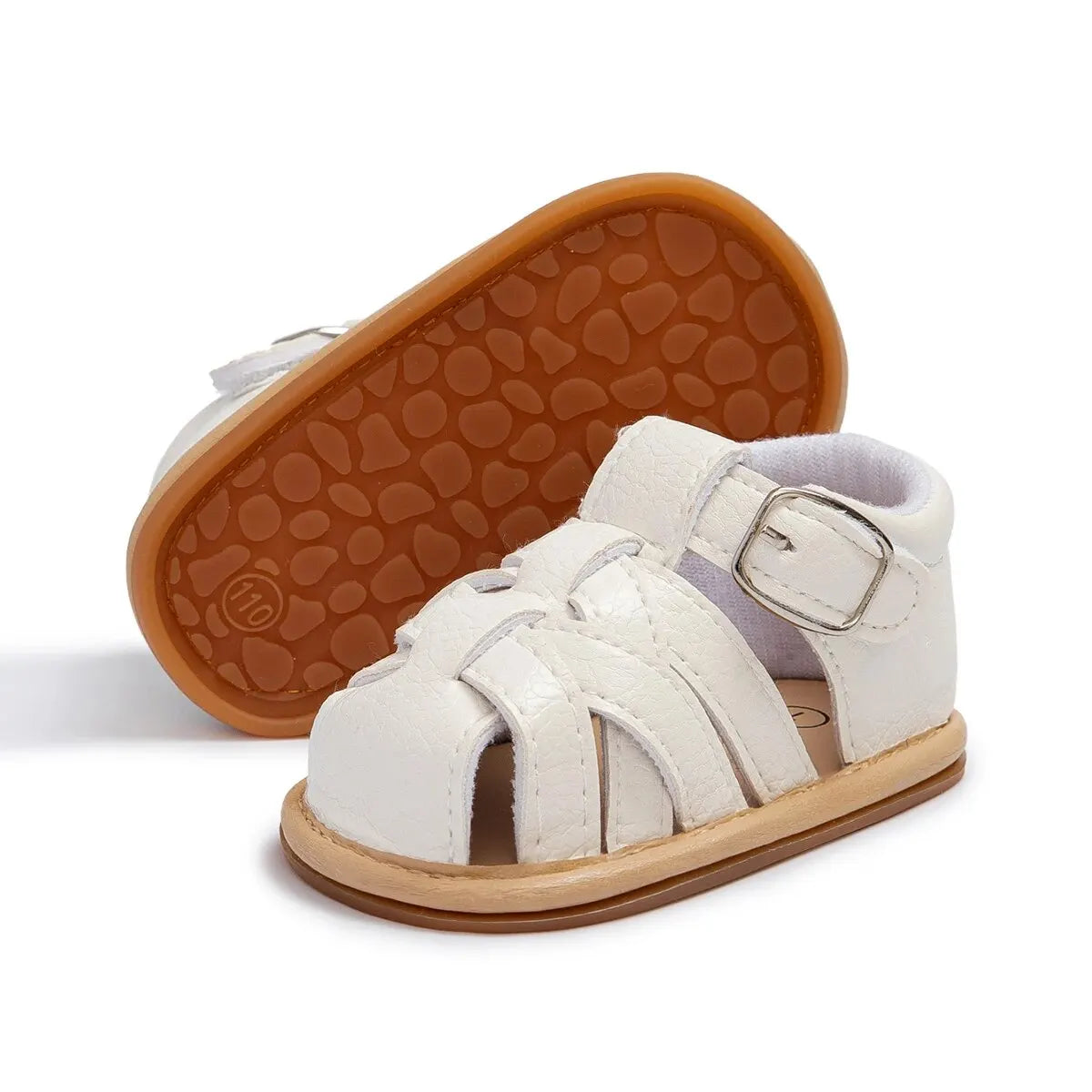 White infant fisherman sandal next to an upturned shoe displaying the textured tan rubber anti-slip outsole.