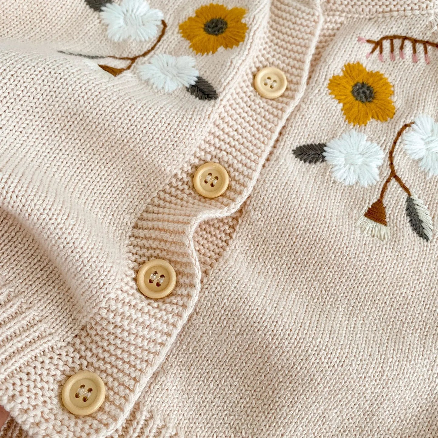 Close-up detail of yellow and white embroidered flowers and wooden buttons on oatmeal knit cardigan.