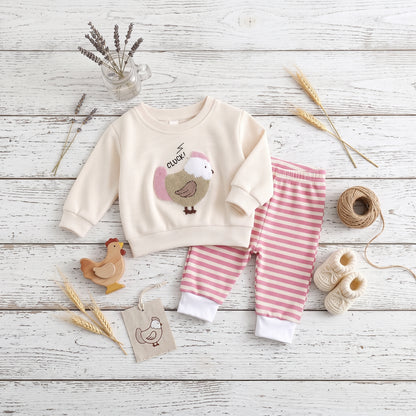 Rustic flat lay of baby girl off-white chicken graphic sweatshirt and pink striped jogger pants set styled on white wood with wooden toys.