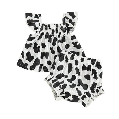 Isolated flat lay of the black and white cow print baby girl two-piece summer set showing the top and shorts.